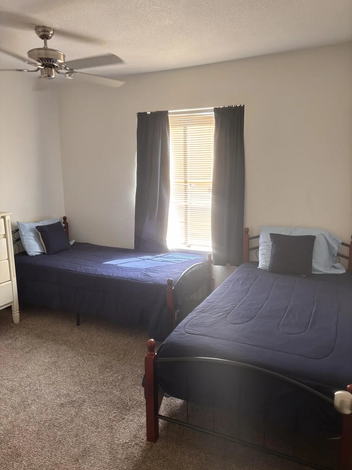 A furnished resident bedroom with two made beds, dresser and ceiling fan