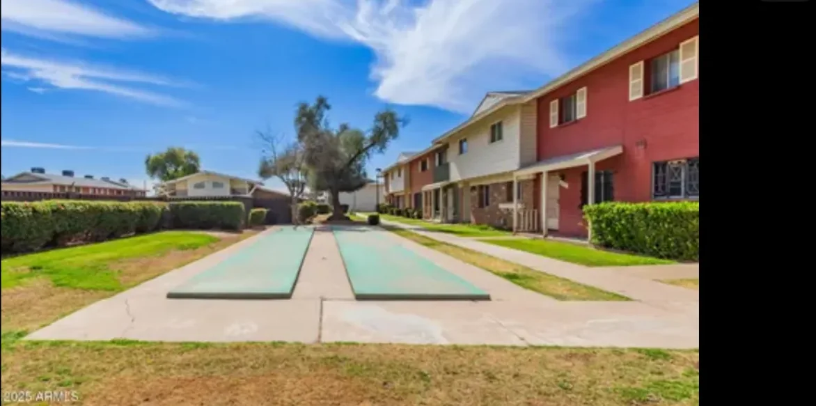 Green shared courtyard between housing buildings under a blue Arizona sky